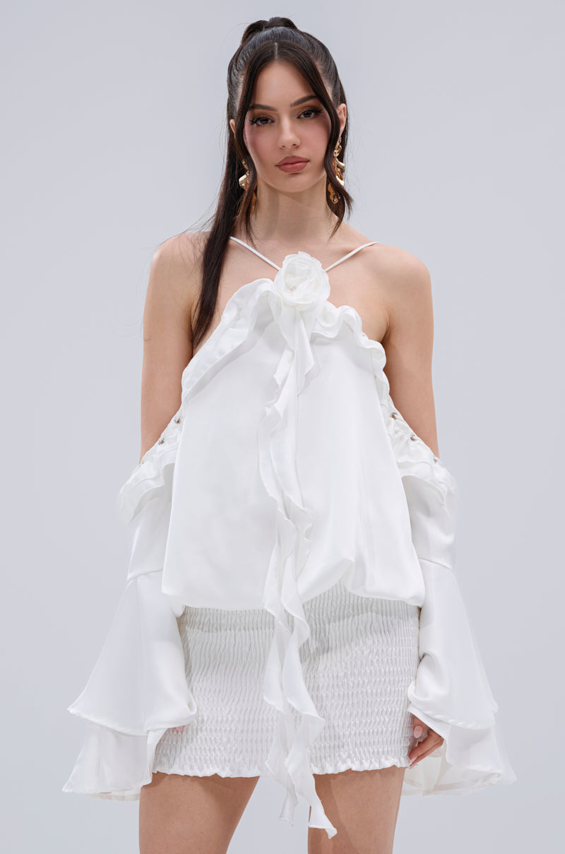 A woman with long dark hair wears the CHIC AF RUFFLE MINI DRESS IN WHITE, featuring ruffled off-the-shoulder sleeves and a white mini skirt, as she stands against a plain light gray background, looking directly at the camera.