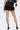 A person stands with their back to the camera, showcasing the LETS FIGHT SATIN SHORT in a high-rise fit, paired with a black cropped top, white ankle boots with black details, and a small black bag for an effortlessly cool streetwear vibe.