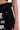 A close-up shows a person wearing the LETS FIGHT SATIN SHORT—shiny black, high-rise shorts with a large satin waist bow and several white embroidered patches, including "LIMITED EDITION." Their hand rests beside them.