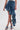 A person models the CRAZY FOR YOU DENIM SKIRT, featuring a dramatic ruffled side and distressed hem, paired with matching denim sandals against a plain light background.