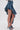 A person wears the CRAZY FOR YOU DENIM SKIRT, featuring a high-low ruffled silhouette with a distressed hem, paired with denim high-heeled sandals. The short front and layered long back stand out against a plain white background.