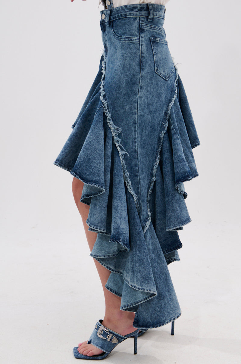 A person wears the CRAZY FOR YOU DENIM SKIRT with a distressed hem, layered ruffled asymmetrical panels, high-low silhouette, and pairs it with matching denim high-heeled sandals for a standout look.