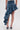 A person wears the CRAZY FOR YOU DENIM SKIRT, featuring a blue asymmetrical high-low silhouette with cascading ruffles on one side and a distressed hem on the other, perfectly paired with high-heeled shoes.