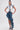 A model wears the CRAZY FOR YOU DENIM SKIRT, an asymmetrical design with a distressed hem and ruffled side, styled with a sleeveless white and denim vest, matching denim sandals, and her hair in a slicked-back high ponytail.