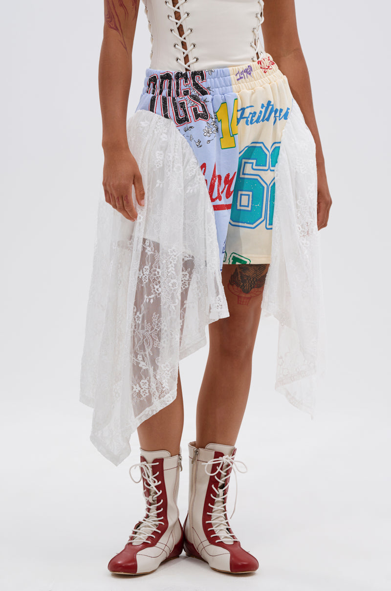 A person wears a white corset top, lace overlay skirt with CARLY LACE GRAPHIC SHORT underneath, and red-and-white lace-up boots. The skirt’s sheer lace panels reveal the vibrant shorts—ideal for festival streetwear. 2