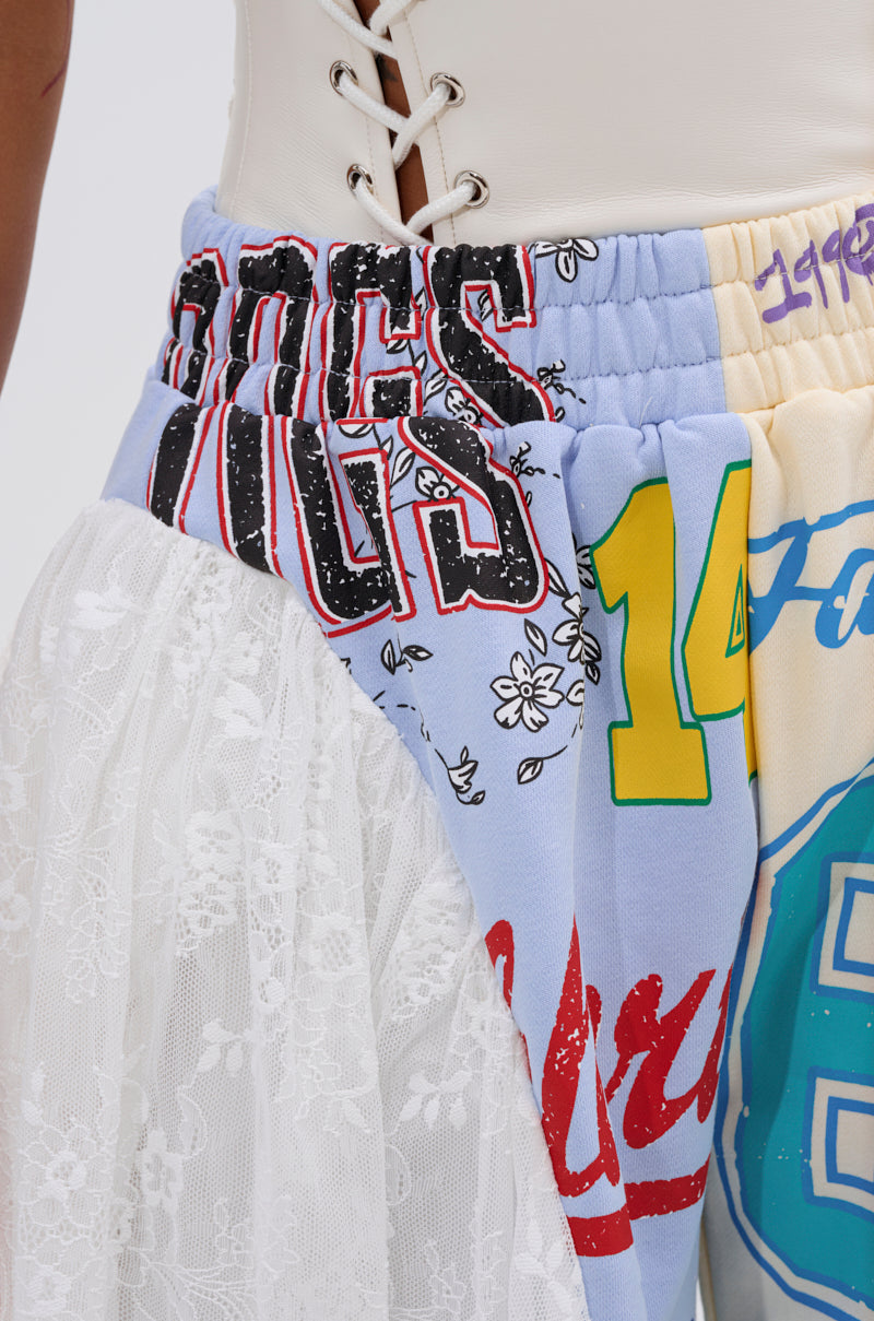 Close-up of a person wearing the CARLY LACE GRAPHIC SHORT and a white lace-up corset top. The shorts showcase lace, bold numbers, flowers, graffiti-style text, and vibrant red, yellow, blue, and white—ideal for festival streetwear. 7
