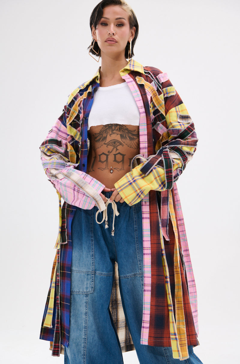 Wearing the DONT EVEN MIXED PLAID LONG BUTTON DOWN over a white crop top and loose blue jeans, a person with a large torso tattoo and short hair confidently poses against a plain background.