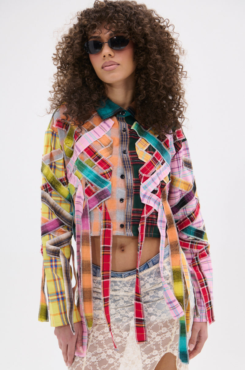 Woman with curly hair and sunglasses wears the FEELING CRAZY MIXED PLAID BUTTON DOWN with long fabric strips and a sheer white lace skirt, standing against a plain white background.