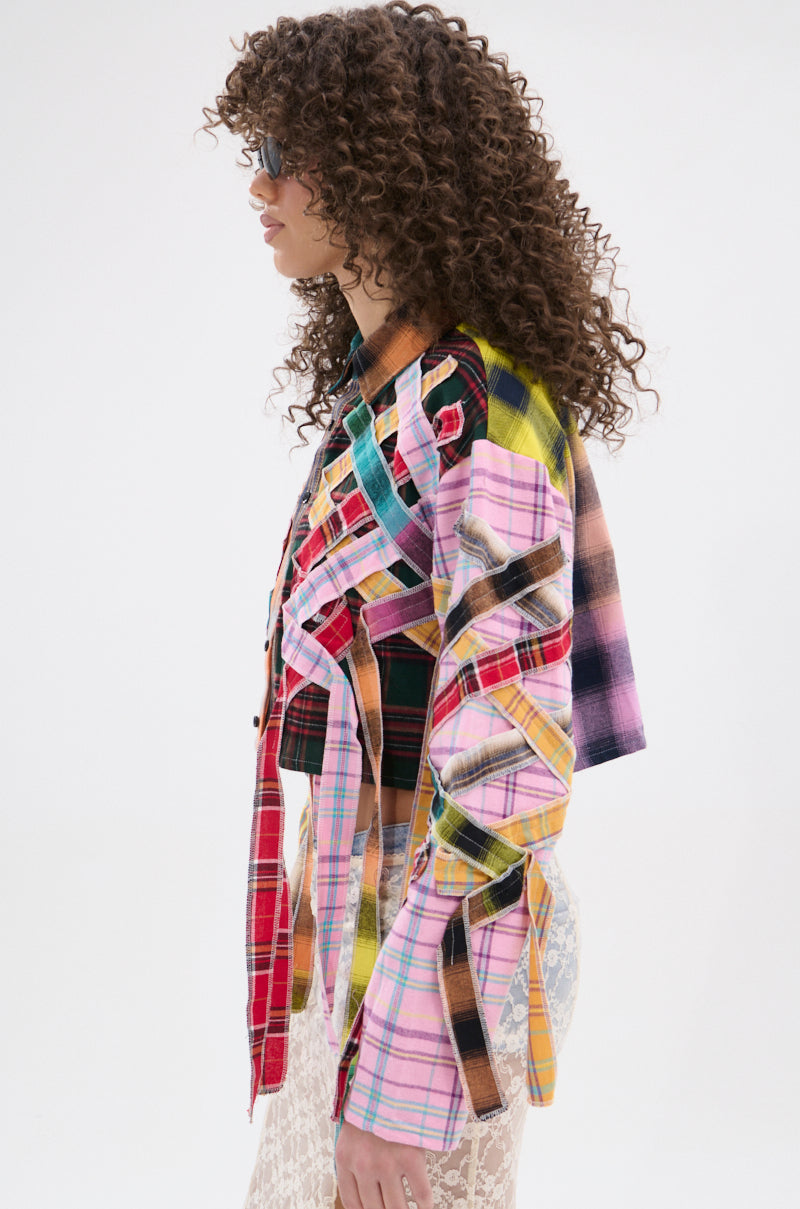 A person with curly hair and sunglasses, seen in profile against a plain white background, wears the FEELING CRAZY MIXED PLAID BUTTON DOWN—a punk-inspired, colorful patchwork shirt with ribbon details.