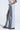 The person is rocking LETS GET IT GOING DISTRESSED JOGGER pants in light gray with brown side panels and a vintage ripped style. Their hands in the pockets enhance their streetwear vibe, paired effortlessly with black platform shoes.