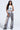 Wearing the LETS GET IT GOING DISTRESSED JOGGER with a strapped sleeveless top and black shoes, the person exudes streetwear flair. Long dark hair and glasses enhance their confident vintage vibe against a plain white background.