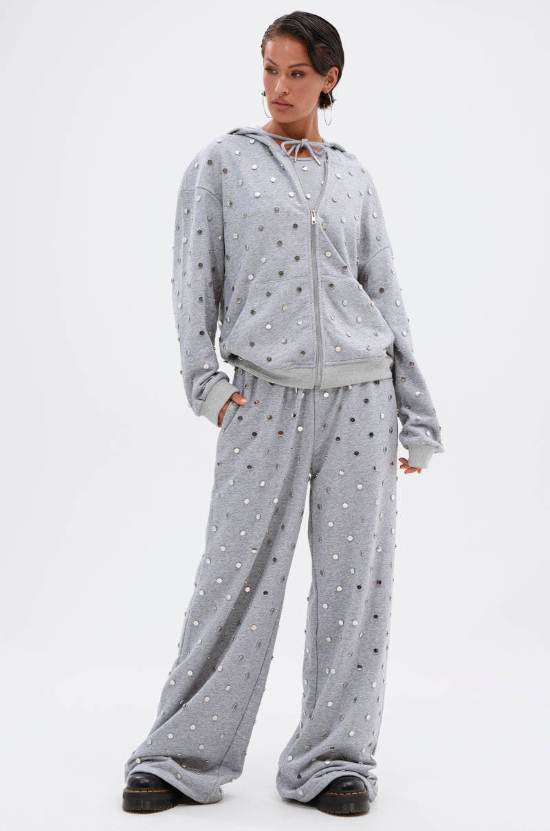A person stands confidently in the POPPING OFF ZIP UP SWEATSHIRT and matching wide-leg pants with metallic polka dots, paired with chunky black shoes against a plain white background.