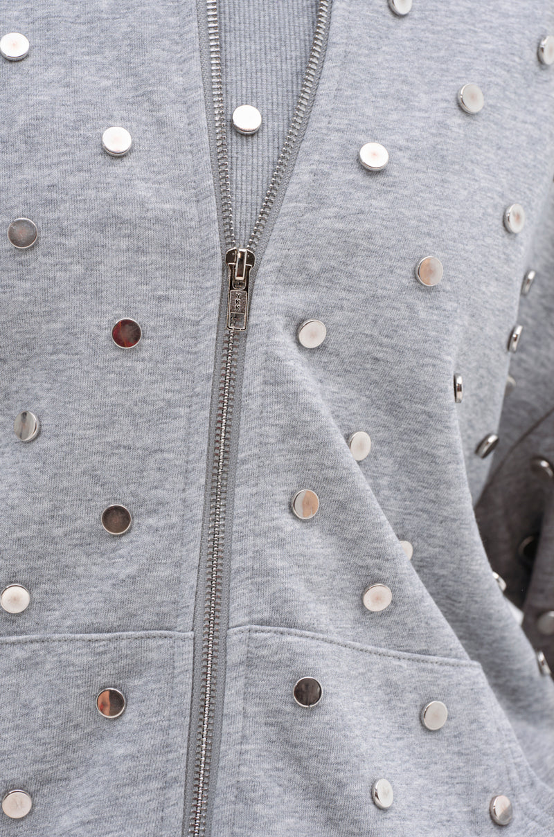 Close-up of the POPPING OFF ZIP UP SWEATSHIRT in light gray, featuring a silver zipper and evenly spaced round silver studs for a stylish, embellished look.