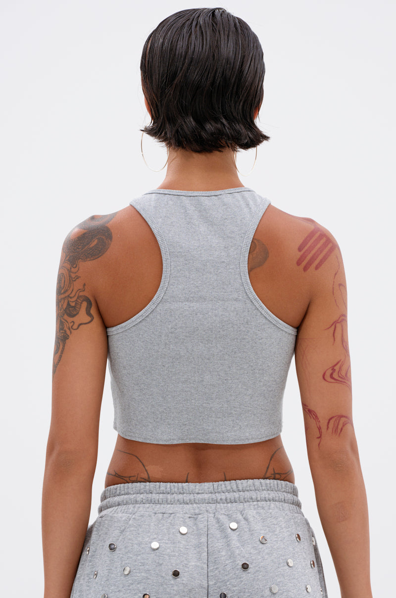 A person with short, dark hair showcases the POPPING OFF TANK—a gray studded tank top—paired with matching sweatpants, both arms covered in tattoos, photographed from the back against a plain light background.