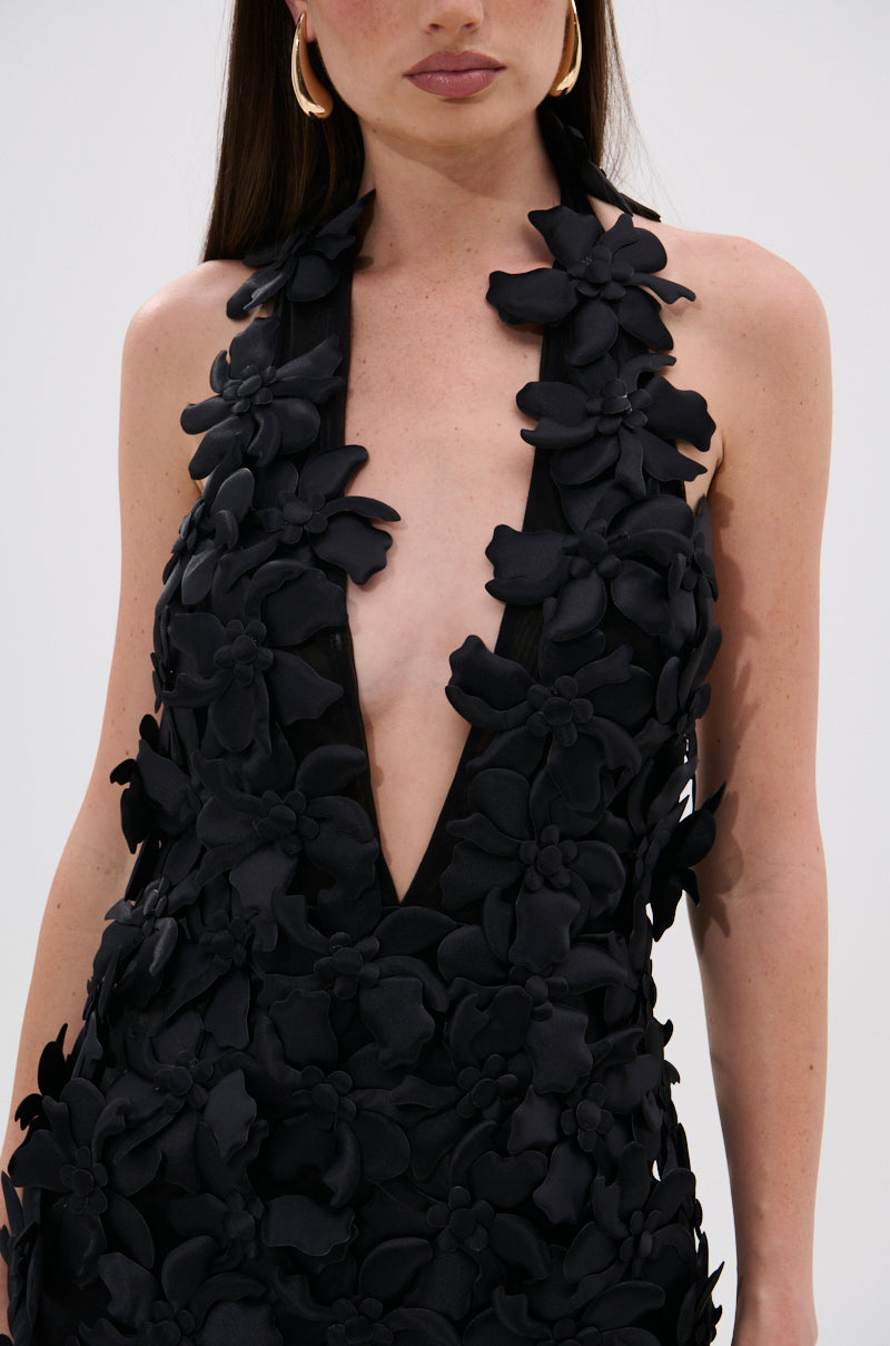 A woman wears the ASHLEY FLORAL MINI DRESS IN BLACK, a mesh halter-style dress with a deep V-neckline and 3D floral appliqués. Only her neck, shoulders, and upper torso are visible.