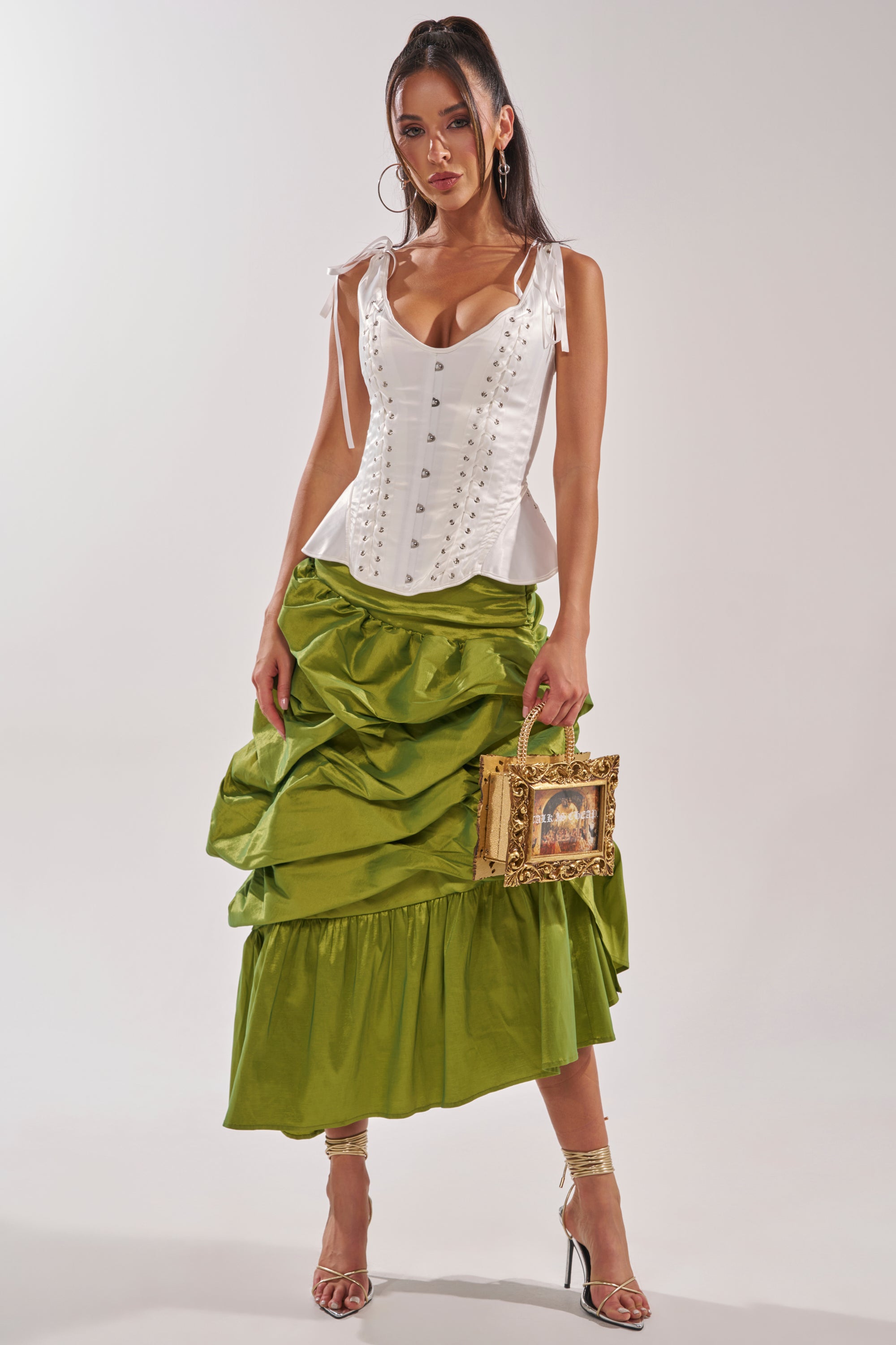 A woman in a white corset top and the ALL OVER THE PLACE MIDI SKIRT in lime green stands holding a box-shaped handbag. She has long dark hair, strappy heels, and poses against a plain background. 6