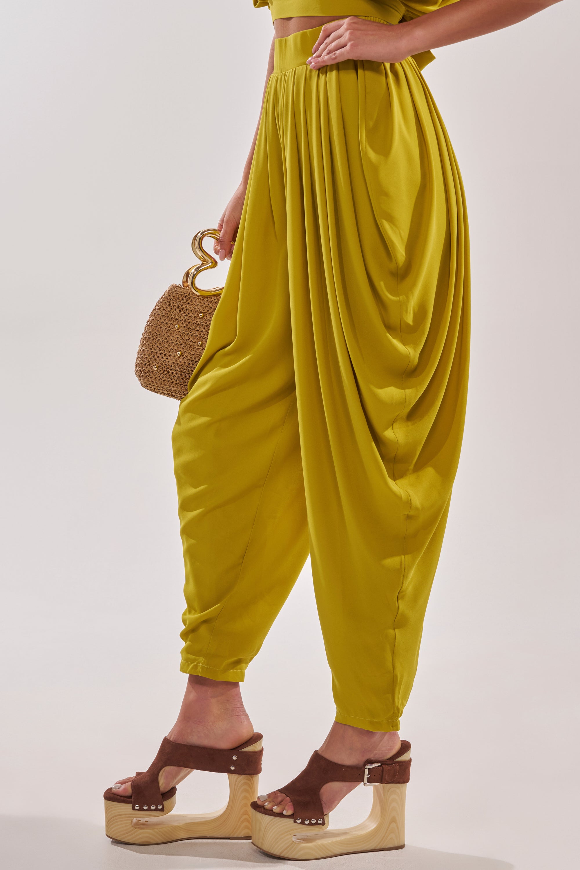 A person wears the READY TO DANCE SLINKY PANT IN CHARTREUSE, styled with brown platform sandals and a small woven handbag—an effortlessly chic resort look photographed against a plain, light background. 3