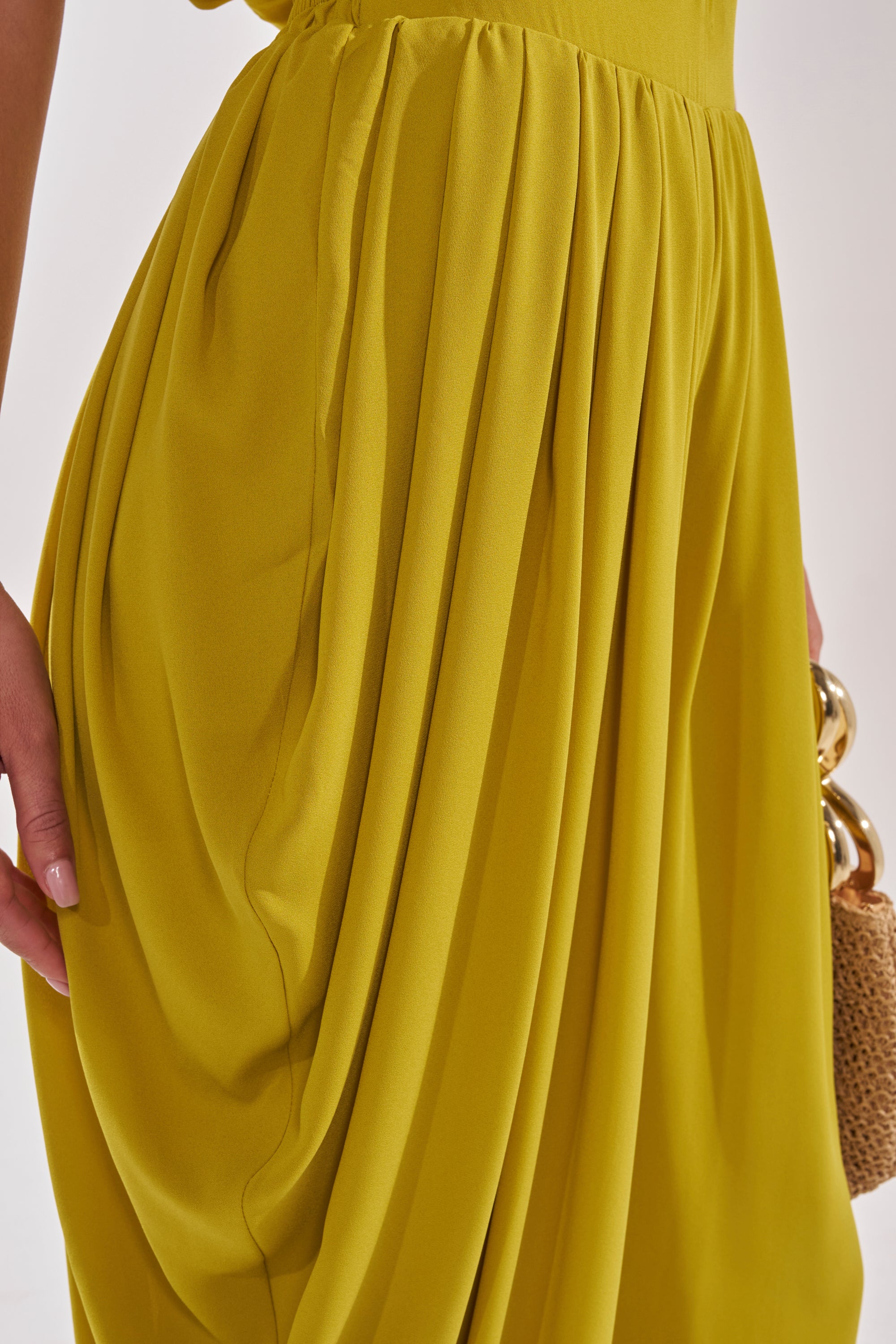 Close-up of a person wearing the READY TO DANCE SLINKY PANT IN CHARTREUSE, featuring soft draping folds and a slightly gathered waist, styled with a small woven handbag with gold circular handles—perfect for resort wear. 7
