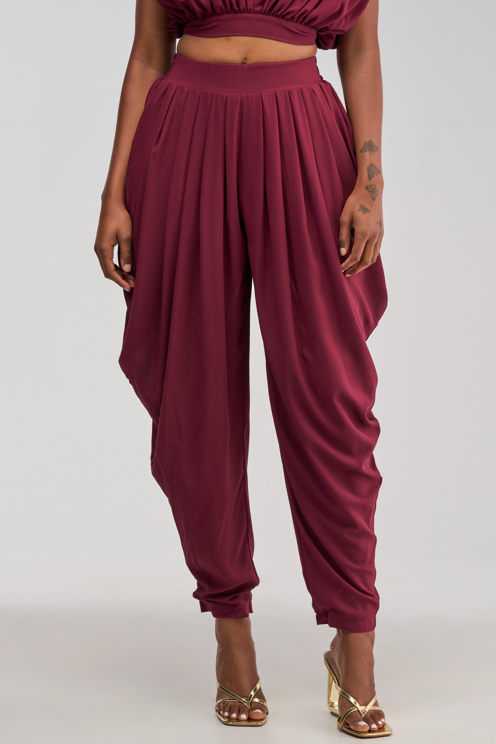 Wearing the READY TO DANCE SLINKY PANT IN BURGUNDY, styled with gold open-toe heels and set against a simple light background, this look effortlessly channels chic resort wear.
