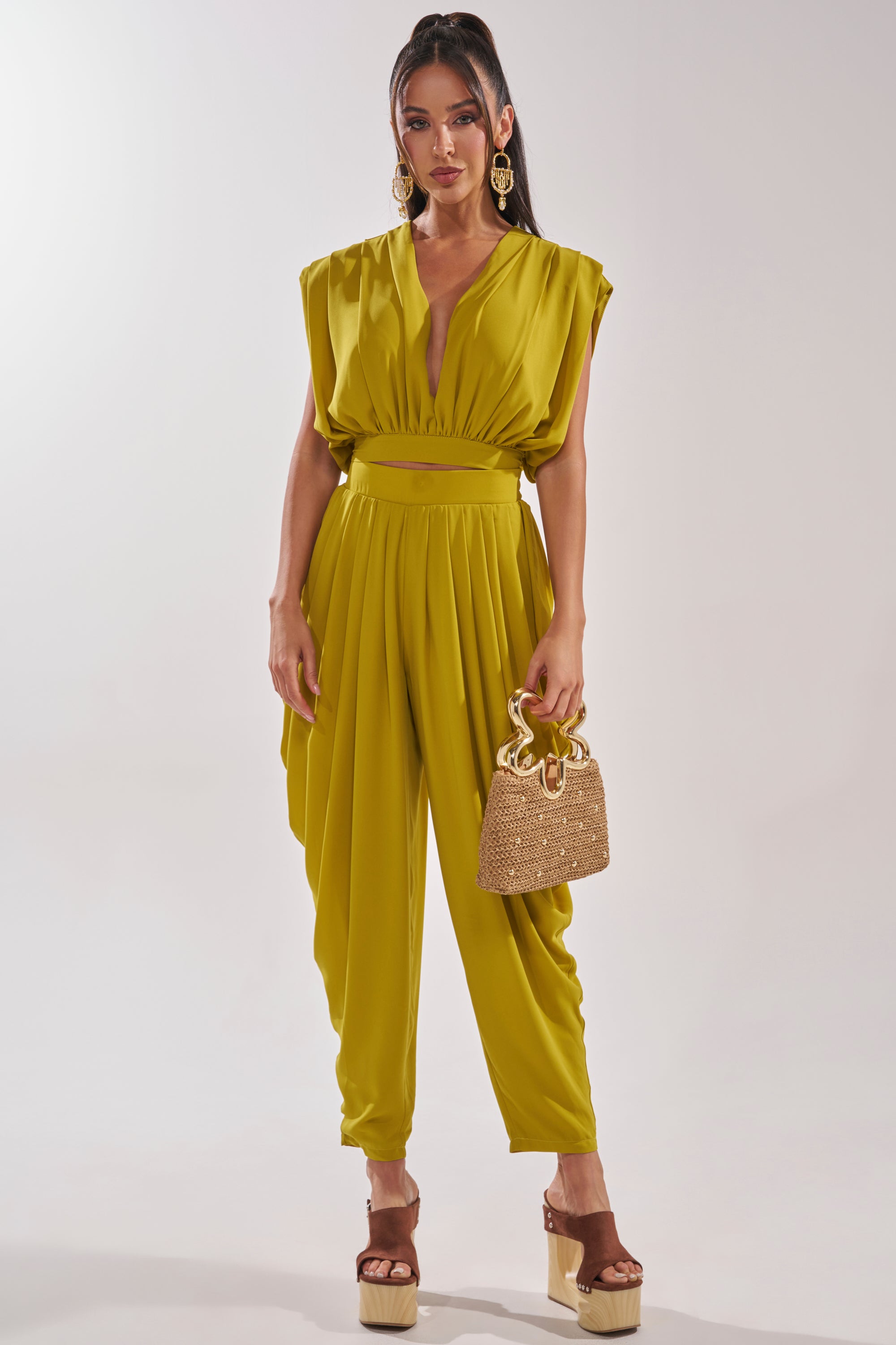 A woman models the READY TO DANCE SLINKY BLOUSE IN CHARTREUSE, styled with wide shoulders and a gathered waist, accessorized with a woven handbag, platform heels, and large gold earrings—ideal for summer events. 5
