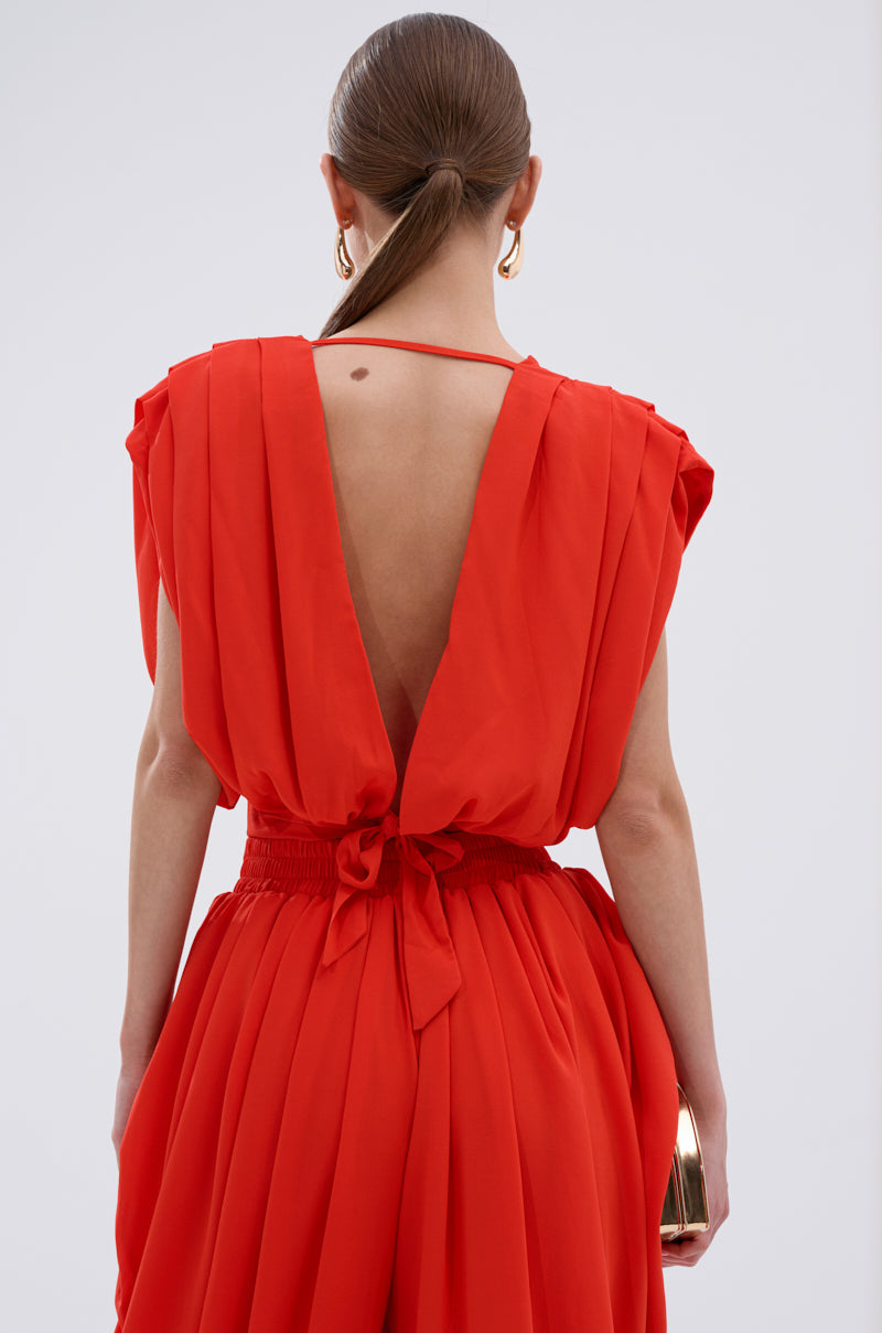 A woman with straight brown hair in a low ponytail wears the READY TO DANCE SLINKY BLOUSE IN ORANGE, paired with large gold hoop earrings and a gold clutch—perfectly styled for a night out. 4
