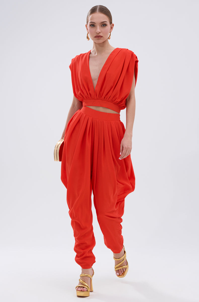 A woman stands confidently against a plain white background, wearing the READY TO DANCE SLINKY BLOUSE IN ORANGE with a deep V-neck and gathered waist—styled perfectly for dancing, paired with a clutch and gold platform sandals. 7