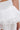 Close-up of a person wearing the MERMAID TAIL MINI SKIRT—a shiny white satin mini with layered ruffles, high waistband, and flared silhouette. The glossy texture stands out as the wearer’s bare arm and small tattoo are visible.