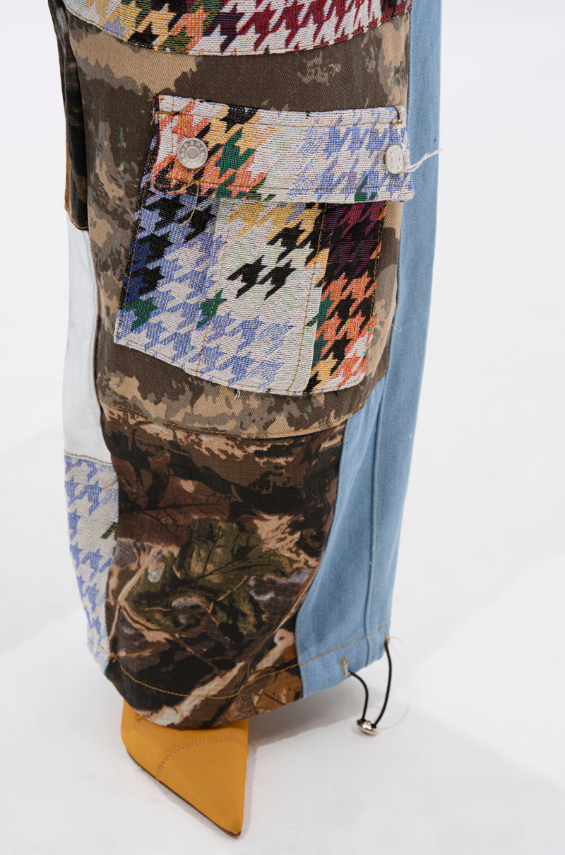 A close-up of the WILD AND FREE DENIM JOGGER showcases patchwork with houndstooth, camouflage, and denim fabrics, a buttoned pocket, and a yellow pointed-toe shoe—ideal for bold streetwear enthusiasts. 11