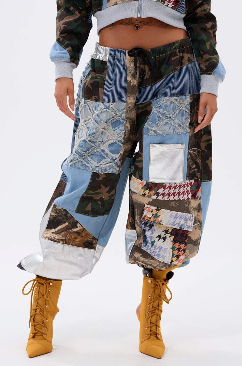 A person wears the WILD AND FREE DENIM JOGGER—patchwork pants featuring denim, camo, and houndstooth—paired with mustard yellow lace-up boots. The upper part of their outfit is partly visible. 2