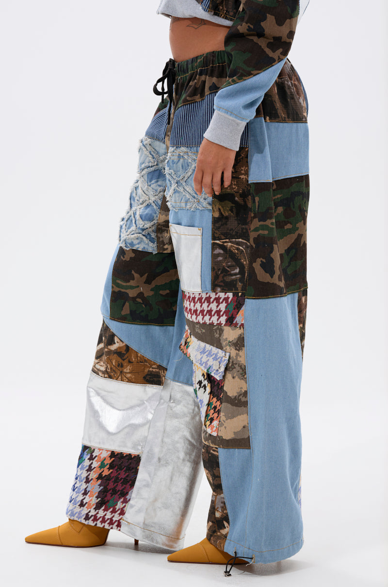 Wearing the WILD AND FREE DENIM JOGGER—patchwork pants featuring denim, camo, houndstooth, metallic, and lace—with a grey cropped top and pointed yellow shoes for a standout streetwear look. 5