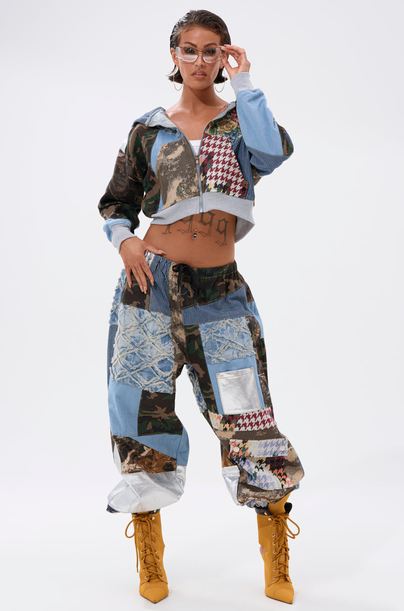 A woman showcases bold streetwear in WILD AND FREE DENIM JOGGER pants with mixed patterns, pairing them with mustard yellow lace-up boots and sunglasses against a plain white background. 8