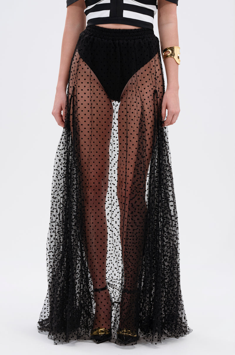 Wearing the MARA SHEER POLKA DOT MAXI SKIRT with a black and white crop top, high-waisted underwear, gold cuff bracelet, and black shoes with gold accents for a chic Parisian-inspired look. Shown from shoulders to feet.