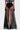A person stands facing away, wearing the MARA SHEER POLKA DOT MAXI SKIRT with high side slits over a black bodysuit. The long skirt reveals legs and is paired with black heels and a stylish black-and-white top.