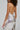 A person with curly hair is wearing the SAMANTHA SEQUIN MIDI DRESS, a sparkling bodycon-style dress adorned with silver and white sequins, featuring adjustable tank straps. They hold a silver clutch bag, and the dress shimmers under the light against a plain, neutral background.