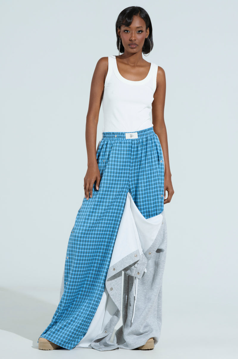 A person wearing the RUNNING LATE JUMPSUIT with a blue checkered and gray mixed pattern design stands against a plain light backdrop.