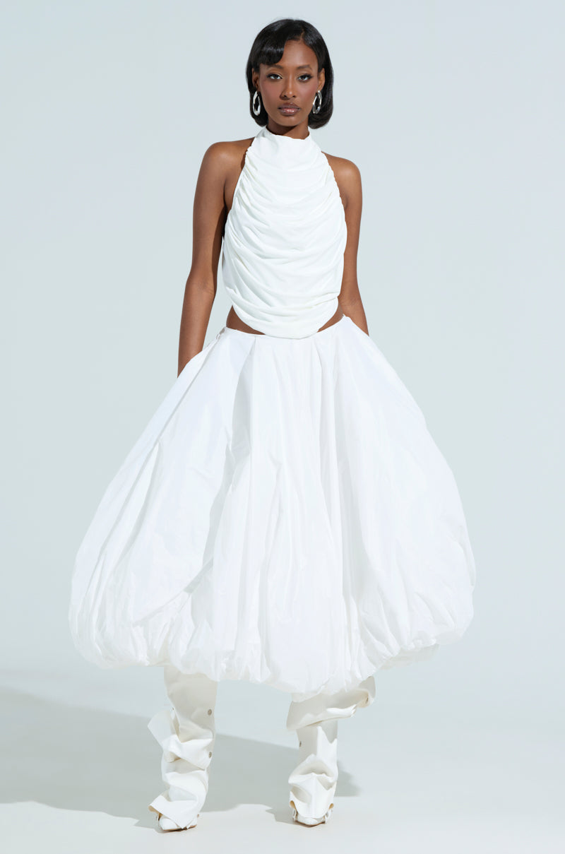 Against a plain background, a person with shoulder-length hair and hoop earrings wears a sleeveless white halter top with ruched detailing and THE BEST MAXI BUBBLE SKIRT in midi length. The look is completed with high-rise white footwear.