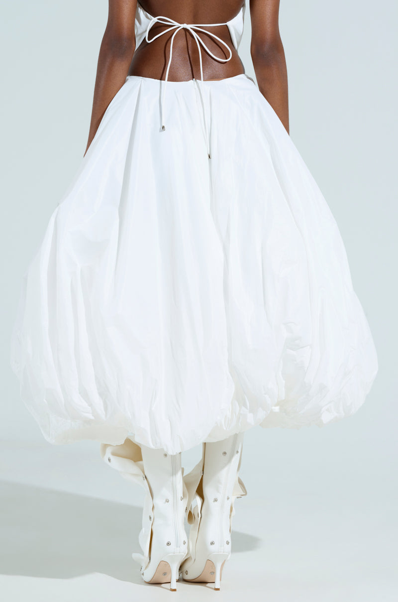 Someone is wearing THE BEST MAXI BUBBLE SKIRT in white, showcasing its voluminous, puffy design from the back. It’s paired with knee-high lace-up white boots on a plain background.
