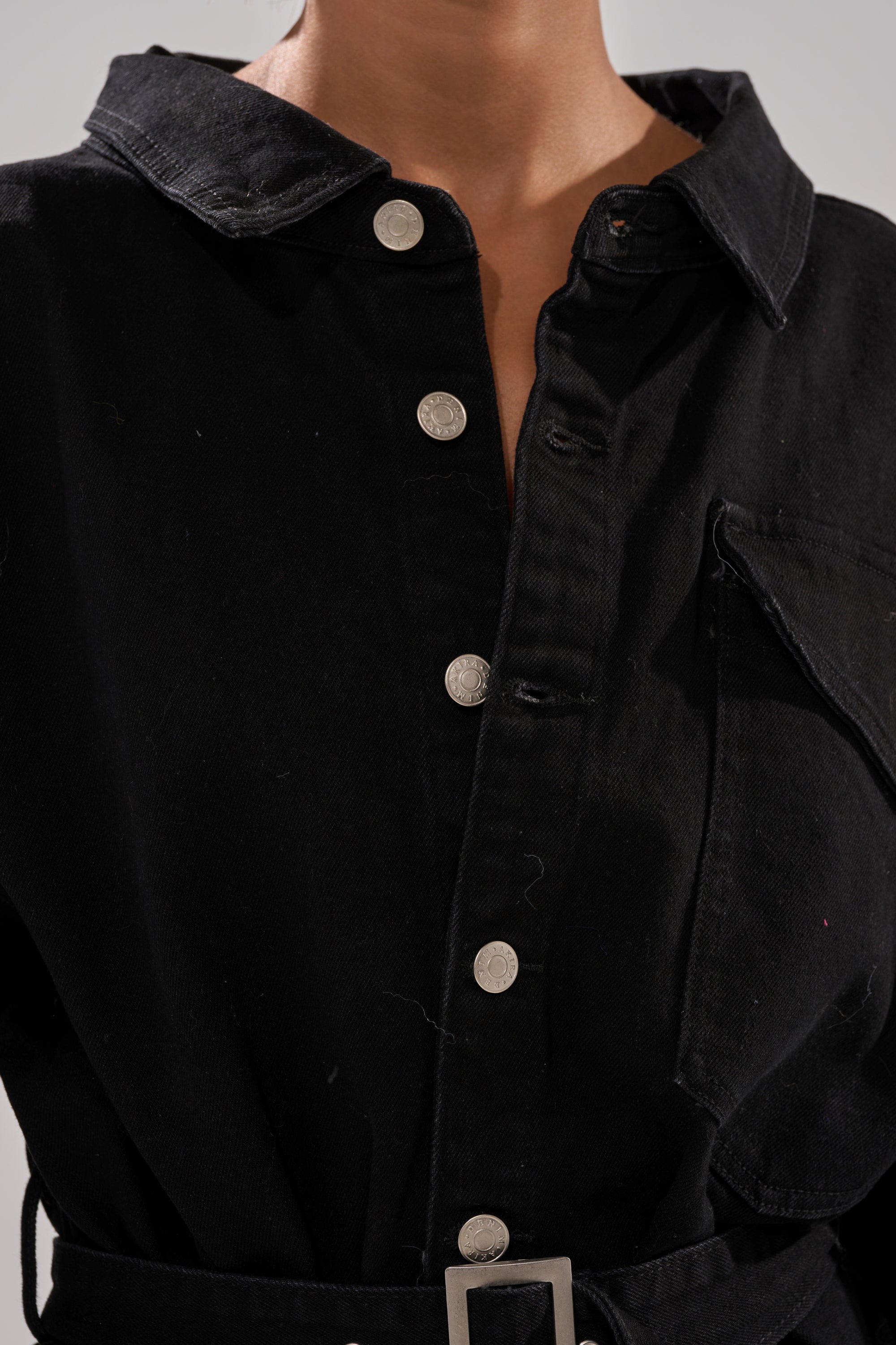 A person is shown from shoulders to waist wearing the PLAY YOUR CARDS RIGHT DENIM JUMPSUIT WITH GROMMETS, featuring a collared button-up top with silver grommet details and chest pocket, paired with wide-leg pants for a stylish look.