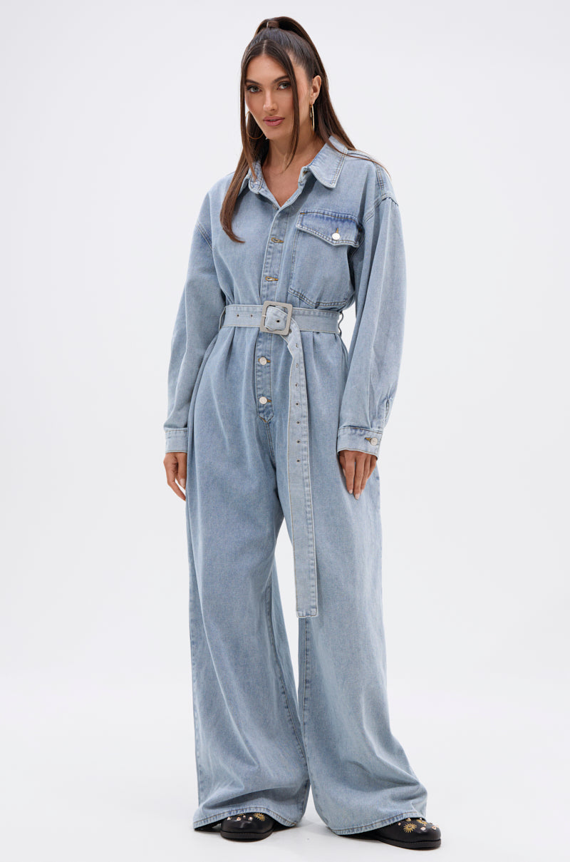 A woman with straight brown hair poses confidently in the NOT TODAY EXTREME OVERSIZED DENIM JUMPSUIT, featuring a wide leg silhouette and adjustable waist belt, against a plain white background.