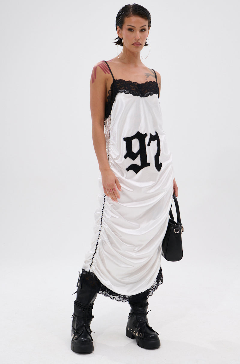 Wearing the GO SPORTS RUCHED MIDI DRESS—a varsity-inspired white slip with black lace trim and "97" on the front—paired with chunky black boots and a small black handbag, they showcase a confident, edgy style.