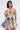 A woman with straight, shoulder-length dark hair models the STAND OUT BROCADE MINI DRESS, a sleeveless floral patchwork mini dress with a fitted bodice and flared skirt, as she looks to the side against a plain light background.