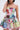 A woman poses in the STAND OUT BROCADE MINI DRESS, a sleeveless, square-neck mini dress featuring a colorful floral patchwork design and flared skirt. She touches her hair, with her face partially out of frame.