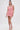 A woman stands against a white background wearing the LEXI FLORAL MINI DRESS, a sleeveless, curve-hugging pink mini dress with 3D floral appliqués and a square neckline, styled with matching open-toe heels and her long dark hair tied back.