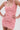 A woman poses with her hands on her hips, wearing the LEXI FLORAL MINI DRESS—a curve-hugging mini dress featuring 3D pink floral appliqués that look like real flowers. The background is plain white.