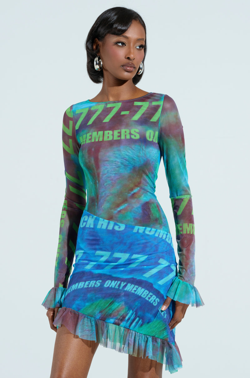 A confident woman stands in a long-sleeve bodycon dress from the AKIRA Label MEMBERS ONLY collection, featuring a digital pattern and "777-77 MEMBERS ONLY" text. The mesh dress has ruffled edges, paired with large hoop earrings against a plain, light-colored backdrop.
