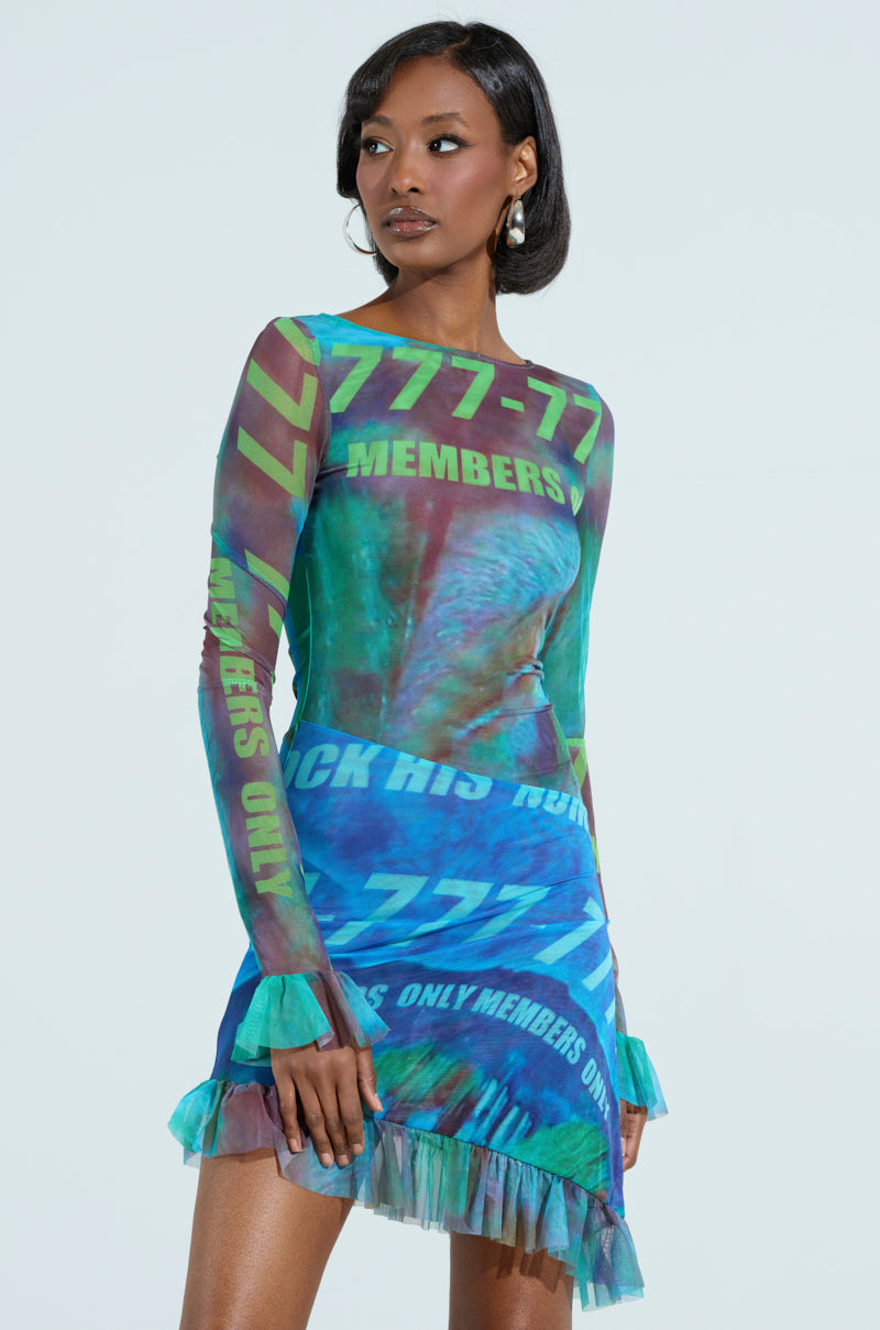Wearing an AKIRA Label MEMBERS ONLY PRINTED MINI DRESS adorned with vibrant "777-77" text patterns and a colorful mix of blue, green, and red hues, a woman complements her short black hair and hoop earrings.