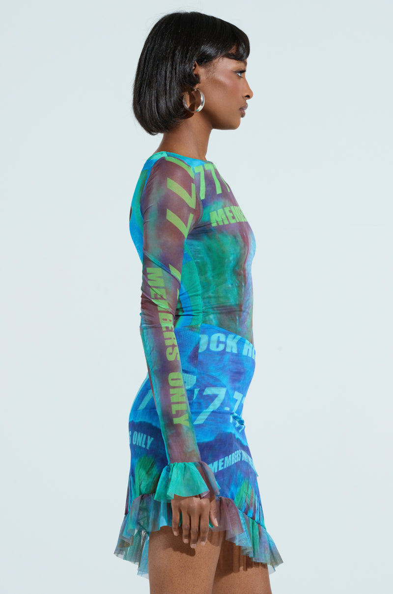The woman is wearing a fitted, multicolored mesh MEMBERS ONLY PRINTED MINI DRESS featuring text patterns and a short ruffled hem. Large hoop earrings and a chic bob complement her look as she stands in profile against a plain background.