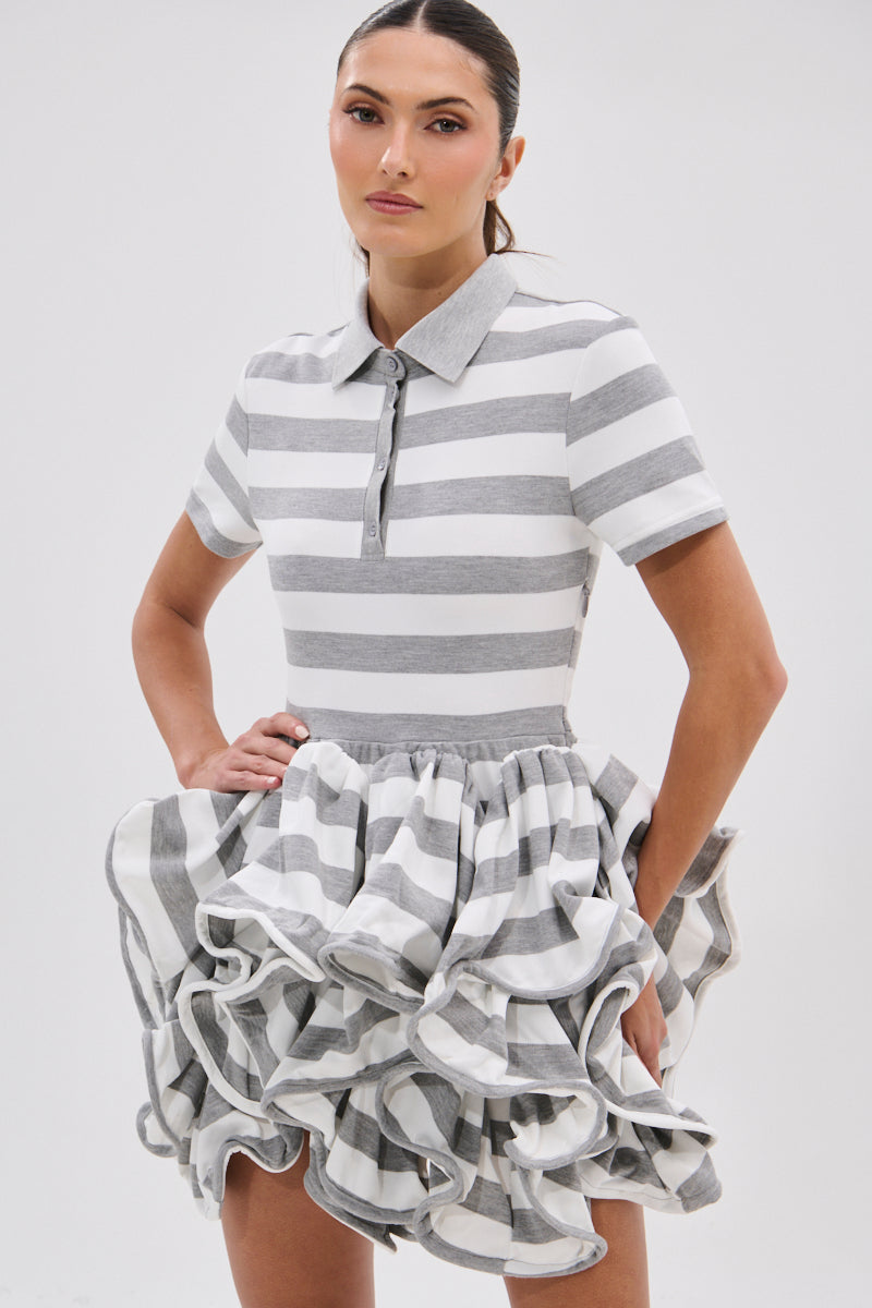 A woman models the OFFICE SIREN STRIPED SHIRT DRESS—featuring gray and white stripes, a collared short-sleeve knit top, and a ruffled bubble skirt—standing against a plain white background.