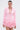 A woman models the STRICTLY BUSINESS BLAZER ROMPER IN PINK—a tailored one-piece with a deep V-neck and ruffled shorts—styled with slicked-back hair and large hoop earrings, set against a plain light background.