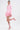 A woman models the STRICTLY BUSINESS BLAZER ROMPER IN PINK—a fitted romper with ruffled hem—paired with pink lace-up heels and hoop earrings against a white backdrop. One leg is bent, arms relaxed for a chic, stylish look.